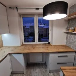 Blat drewniany w kuchni w Malborku, z widokiem na ośnieżone budynki za oknem, oświetlony wiszącą lampą z czarnym abażurem.