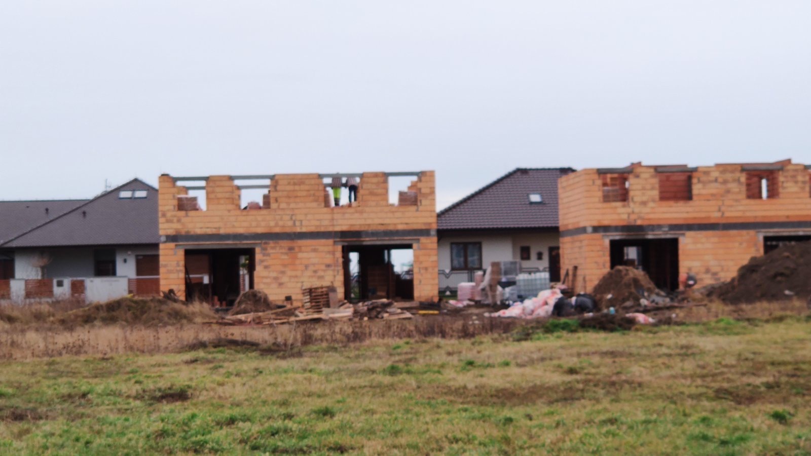 Wczesny etap budowy dwóch domów jednorodzinnych z pustaków ceramicznych; widoczne zbrojenia i przygotowane otwory okienne.