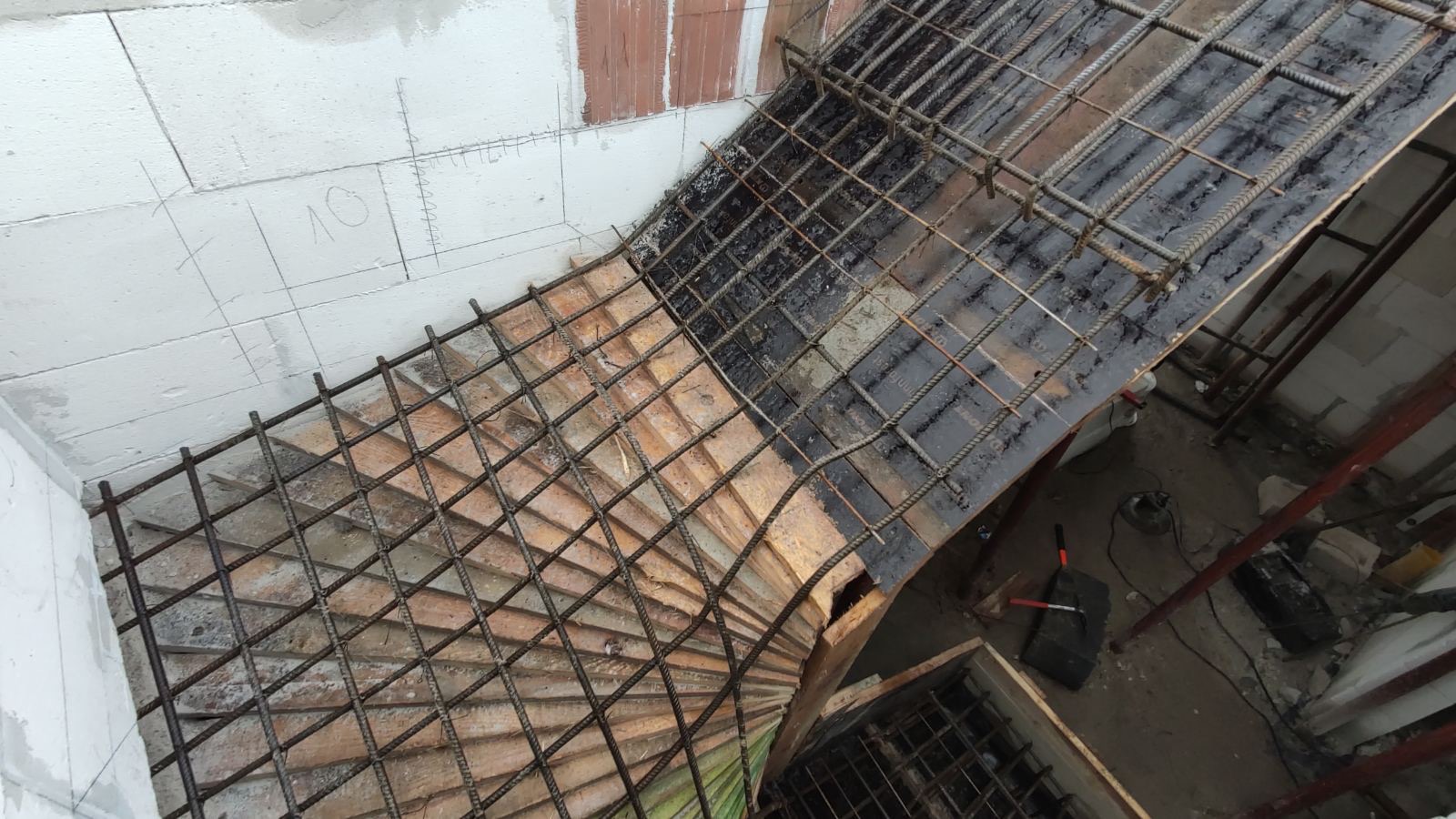 Zbrojenie schodów z siatki stalowej na deskowaniu, widok z góry na placu budowy, z zaznaczonymi liniami na ścianie.