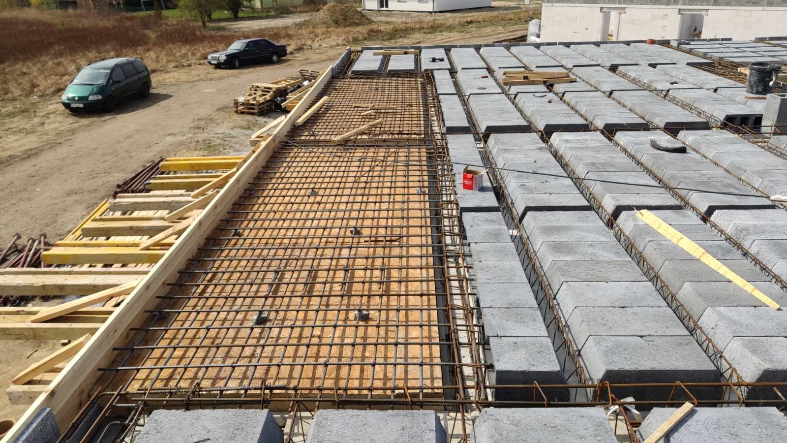 Wykonywanie stropu Teriva: szalunek zbrojony siatką stalową i ułożone pustaki stropowe, widoczne elementy drewniane szalunku i samochody w tle.