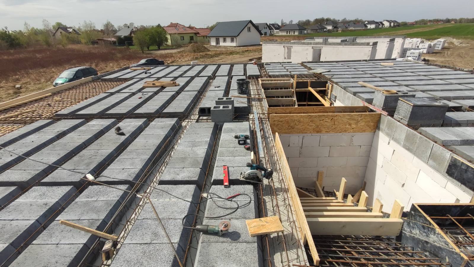 Budowa stropu Teriva: widok z góry na ułożone pustaki stropowe i zbrojenie, narzędzia pracy na wierzchu, w tle budynki mieszkalne.