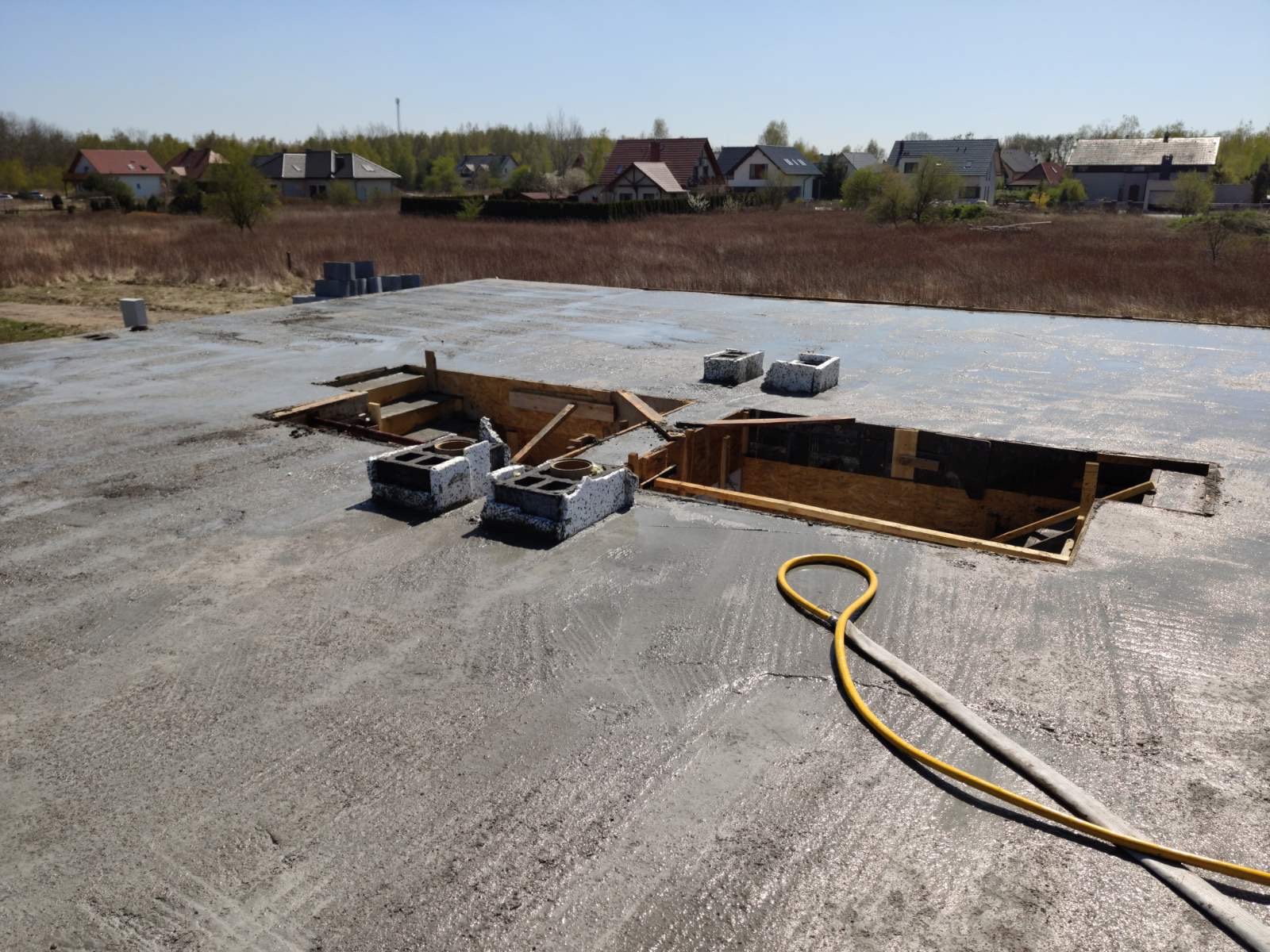 Wylewka fundamentowa w trakcie realizacji we Wrocławiu, widoczne otwory na instalacje, żółty wąż do pompy betonu i bloczki betonowe.