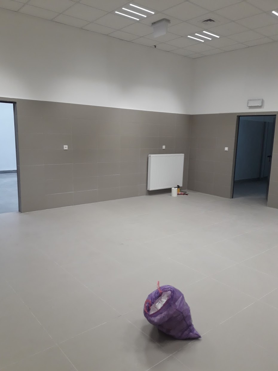 Wykafelkowane pomieszczenie z grzejnikiem, workiem na śmieci i otwartymi drzwiami, po remoncie, widoczne narzędzia malarskie.