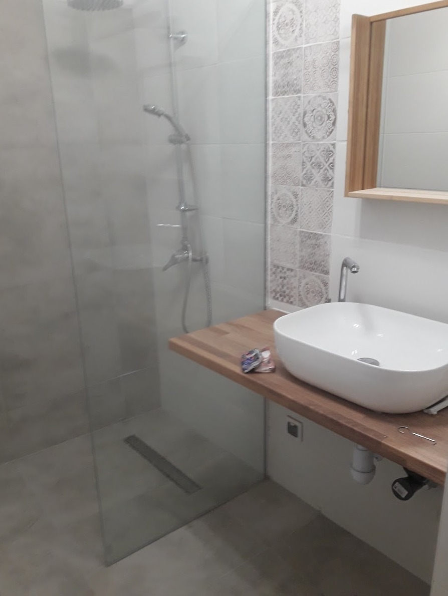 Nowoczesna łazienka po remoncie: kabina prysznicowa ze szklaną ścianką, drewniany blat z umywalką nablatową, płytki dekoracyjne w pionowym pasie.