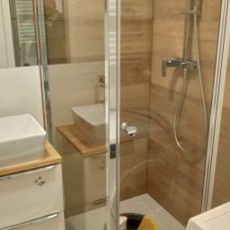 Mateusz Rokita - Nowoczesna kabina prysznicowa z drewnopodobnymi płytkami, widoczny fragment umywalki i szafki, wiadro z detergentami w brodziku, prawdopodobnie w trakcie sprzątania po remoncie.