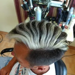 Męska fryzura z kontrastowym, platynowym pasem na górze, widok z góry, w tle półka z kosmetykami i akcesoriami.