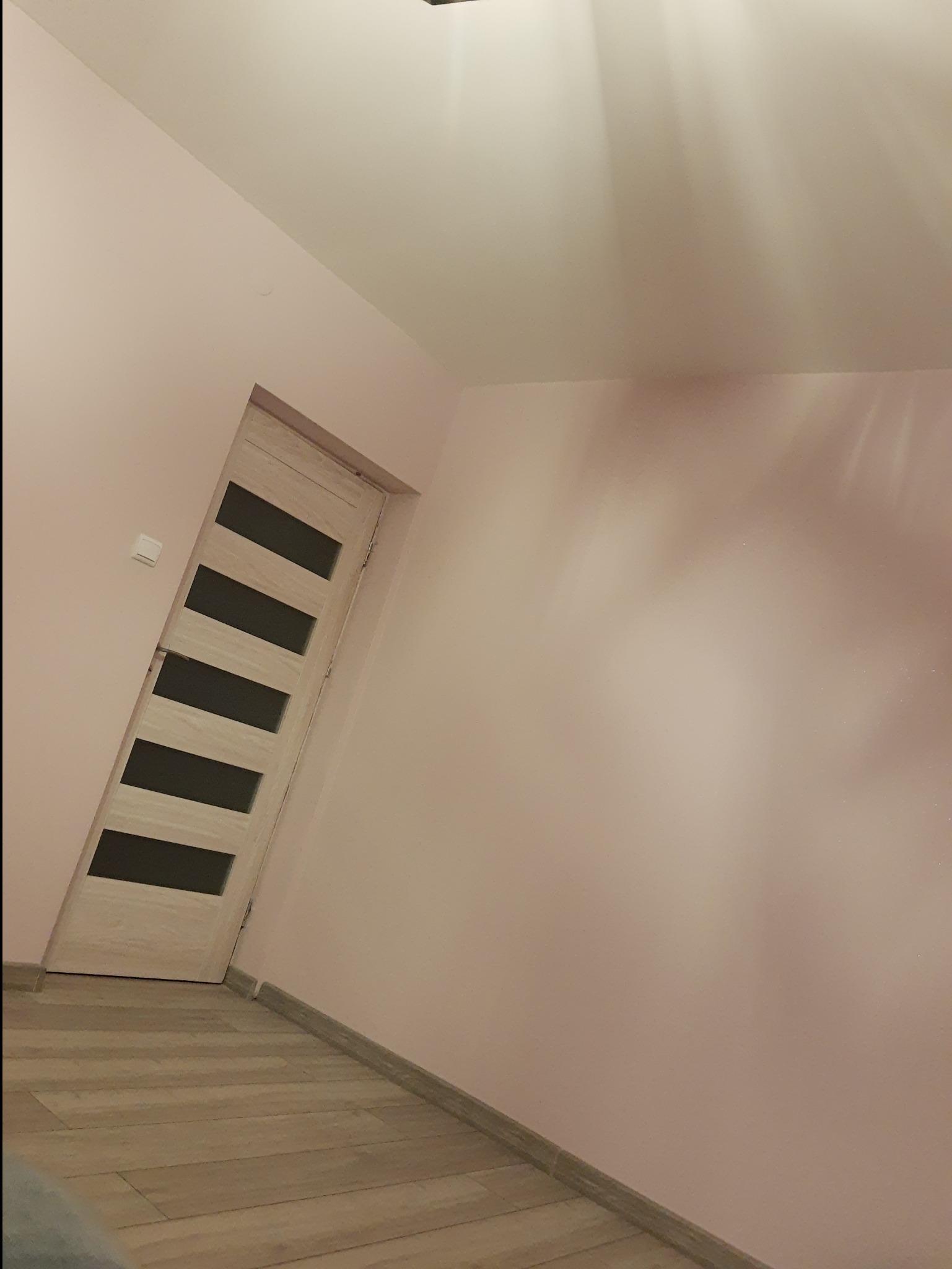 Ściana pomalowana na różowo, drewnopodobne panele podłogowe i drzwi z poziomymi, ciemnymi wstawkami.