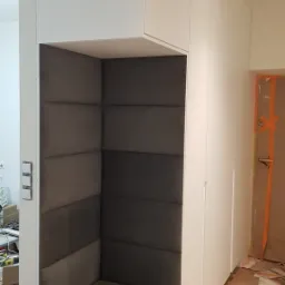 Wnęka z tapicerowanym siedziskiem i ścianami w zabudowie meblowej w Izabeli, widoczne ślady prac wykończeniowych na podłodze.