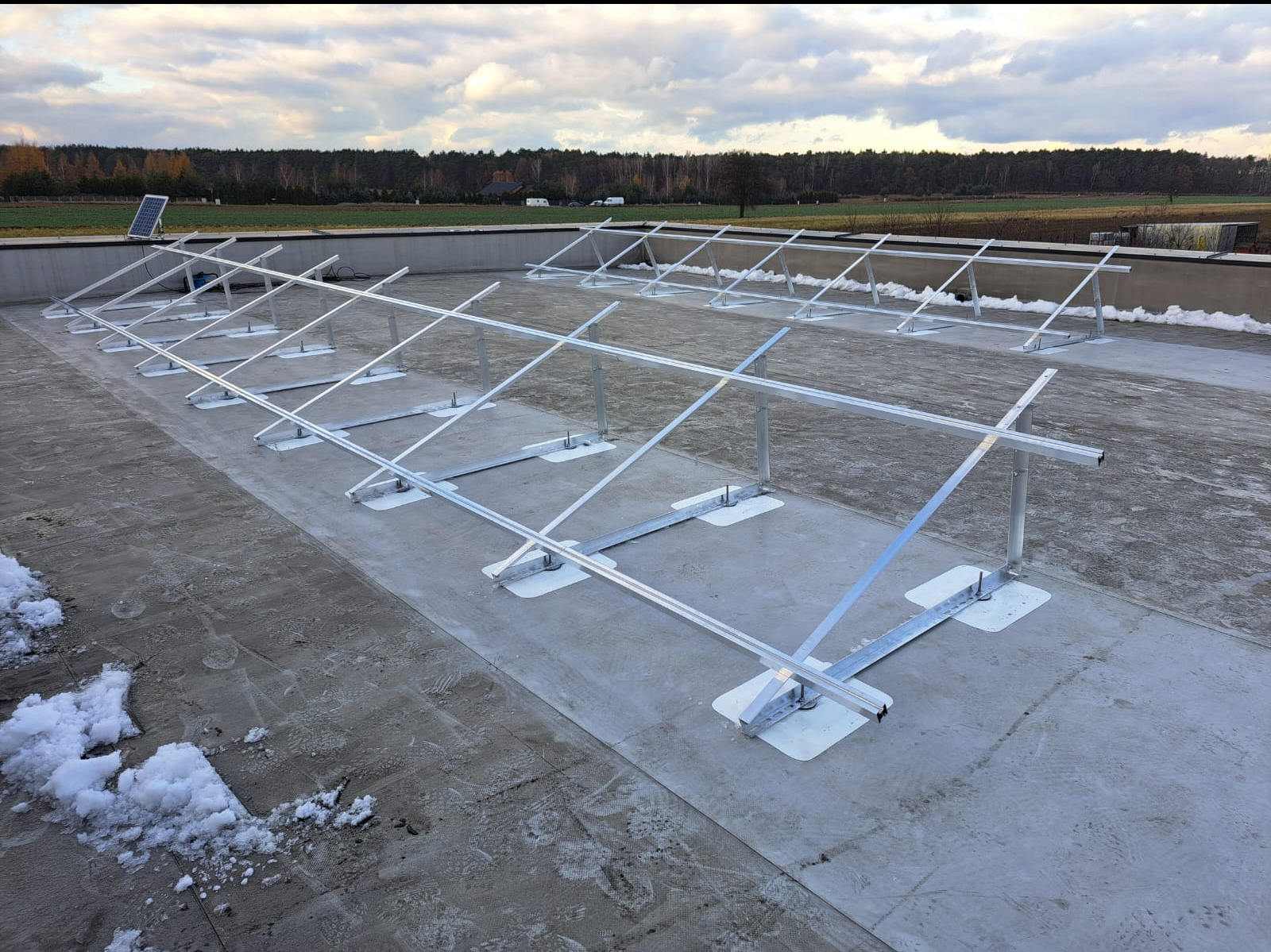 Montaż stelażu pod panele słoneczne na płaskim dachu, widoczne elementy mocujące i odśnieżony fragment dachu