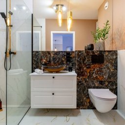 High Standard  - wykończenia wnętrz - Nowoczesna łazienka z marmurowymi płytkami, szklaną kabiną prysznicową z czarną armaturą, umywalką w kształcie misy na białej szafce i wiszącą toaletą.