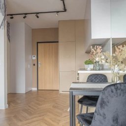 High Standard  - wykończenia wnętrz - Jasne wnętrze mieszkania z parkietem w jodełkę, czarnymi krzesłami i dekoracyjną tapetą z motywem roślinnym.