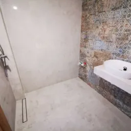 Nowoczesna łazienka z kabiną prysznicową typu walk-in, wykończona płytkami w odcieniach szarości i dekoracyjnymi płytkami z motywem patchworkowym przy umywalce nablatowej.