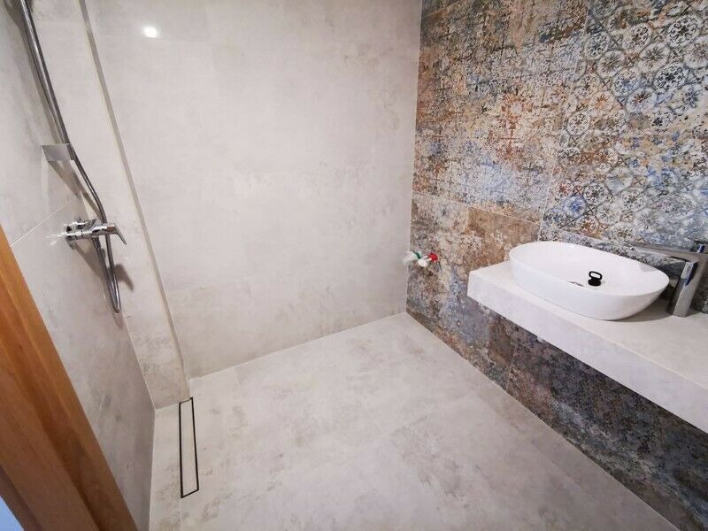 Nowoczesna łazienka z kabiną prysznicową typu walk-in, wykończona płytkami w odcieniach szarości i dekoracyjnymi płytkami z motywem patchworkowym przy umywalce nablatowej.