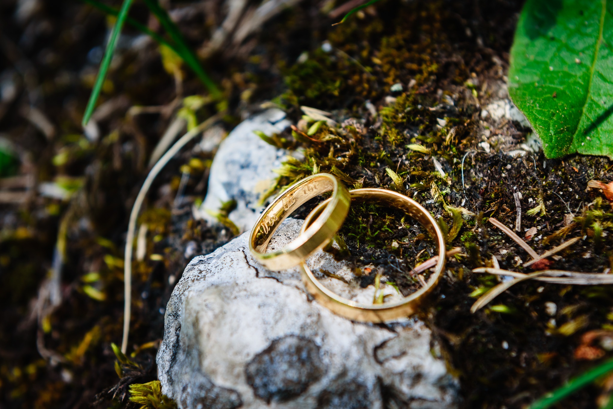 Dwa złote pierścionki ślubne leżące na kamieniu porośniętym mchem, z inskrypcją widoczną na jednym z nich.