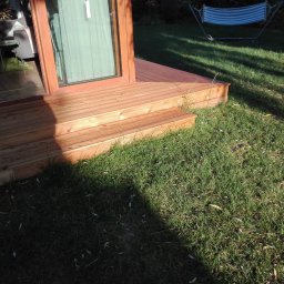 Parkiety Schody Tarasy Mirosław Rokicki - Drewniany taras z niskimi schodami prowadzący do przeszklonych drzwi. W tle trawnik i hamak.