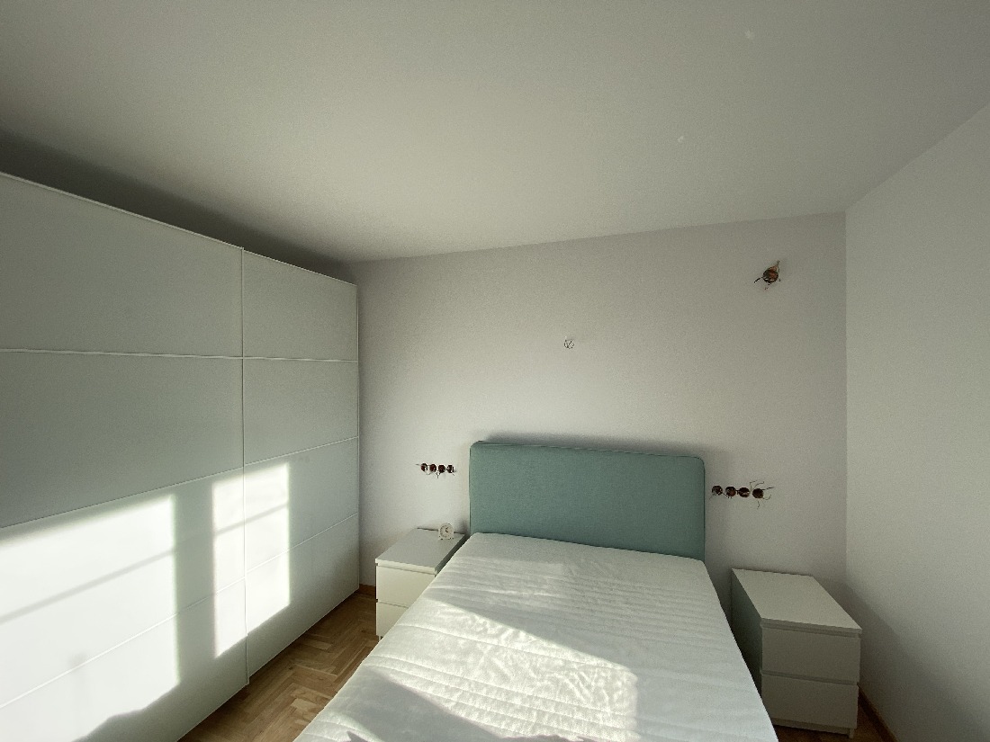 Pokój w trakcie wykańczania: białe ściany z wystającymi kablami, łóżko z turkusowym zagłówkiem, szafa przesuwna i niedokończone gniazdka elektryczne.