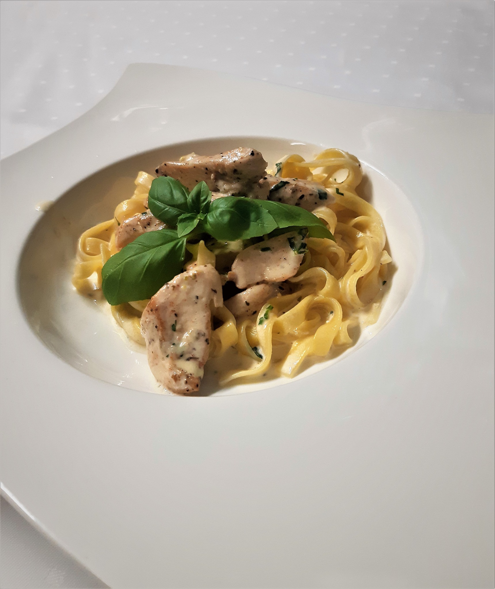 Elegancko podane tagliatelle z kurczakiem w kremowym sosie, udekorowane świeżą bazylią, na białym, designerskim talerzu