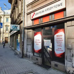 Fasada Centrum Kredytowego z ofertami kredytów gotówkowych, hipotecznych, firmowych i chwilówek, widoczny szyld z godzinami otwarcia i numerem telefonu, obok budynek banku CA i pusta ulica...