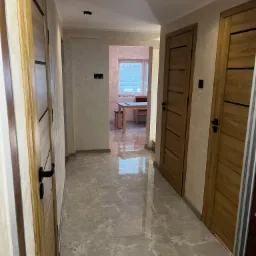 Korytarz w mieszkaniu z trzema drewnianymi drzwiami z czarnymi akcentami, wykończony płytkami imitującymi marmur.