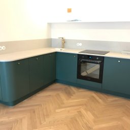 ARCHANS ARKADIUSZ KANIA - Nowoczesna kuchnia z zielonymi szafkami, jasnym blatem i drewnianą podłogą w jodełkę; widoczny piekarnik i złota bateria.