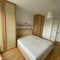 ARCHANS ARKADIUSZ KANIA - Nowoczesna sypialnia z łóżkiem z rattanowym wezgłowiem, szafą z frontami z plecionki rattanowej i drewnianą podłogą.