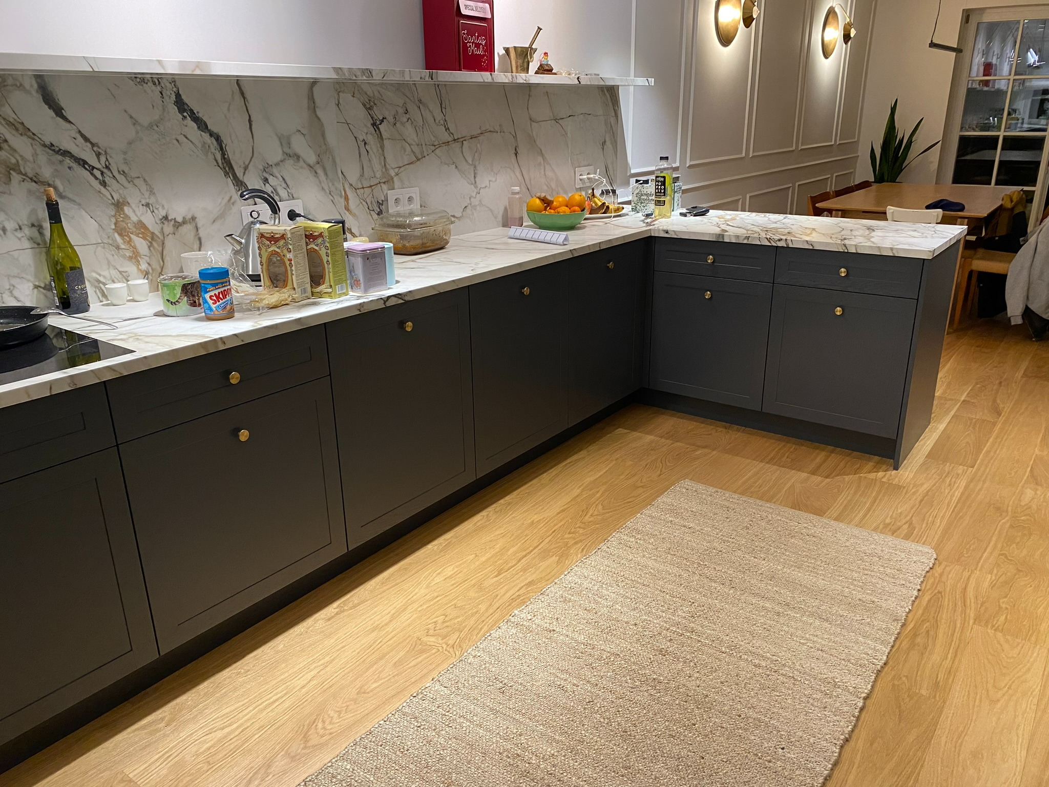 Nowoczesna kuchnia w Warszawie z szarymi szafkami i blatem imitującym marmur, uzupełniona o drewnianą podłogę i dywan.