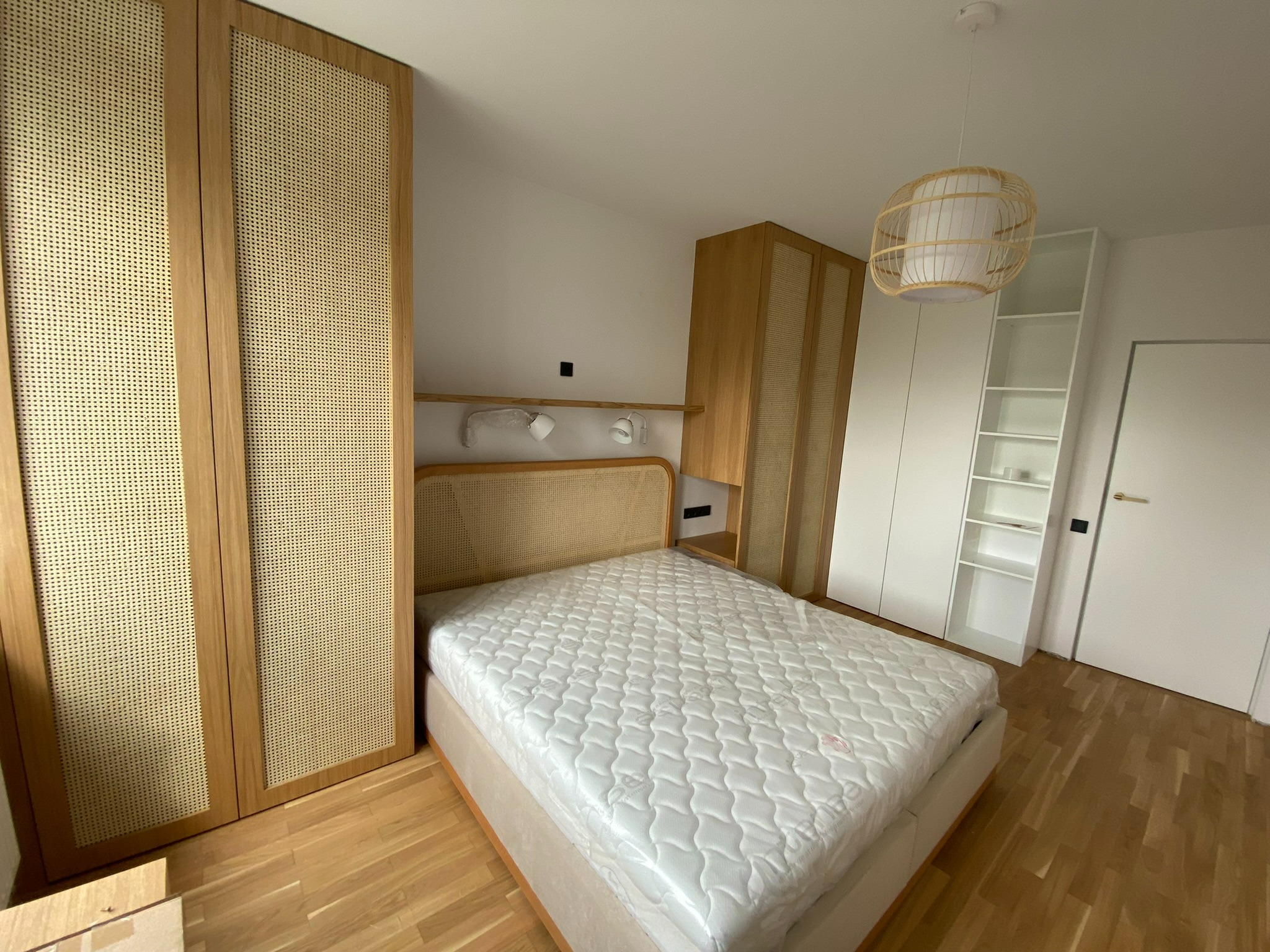 Nowoczesna sypialnia z łóżkiem z rattanowym wezgłowiem, szafą z frontami z plecionki rattanowej i drewnianą podłogą.