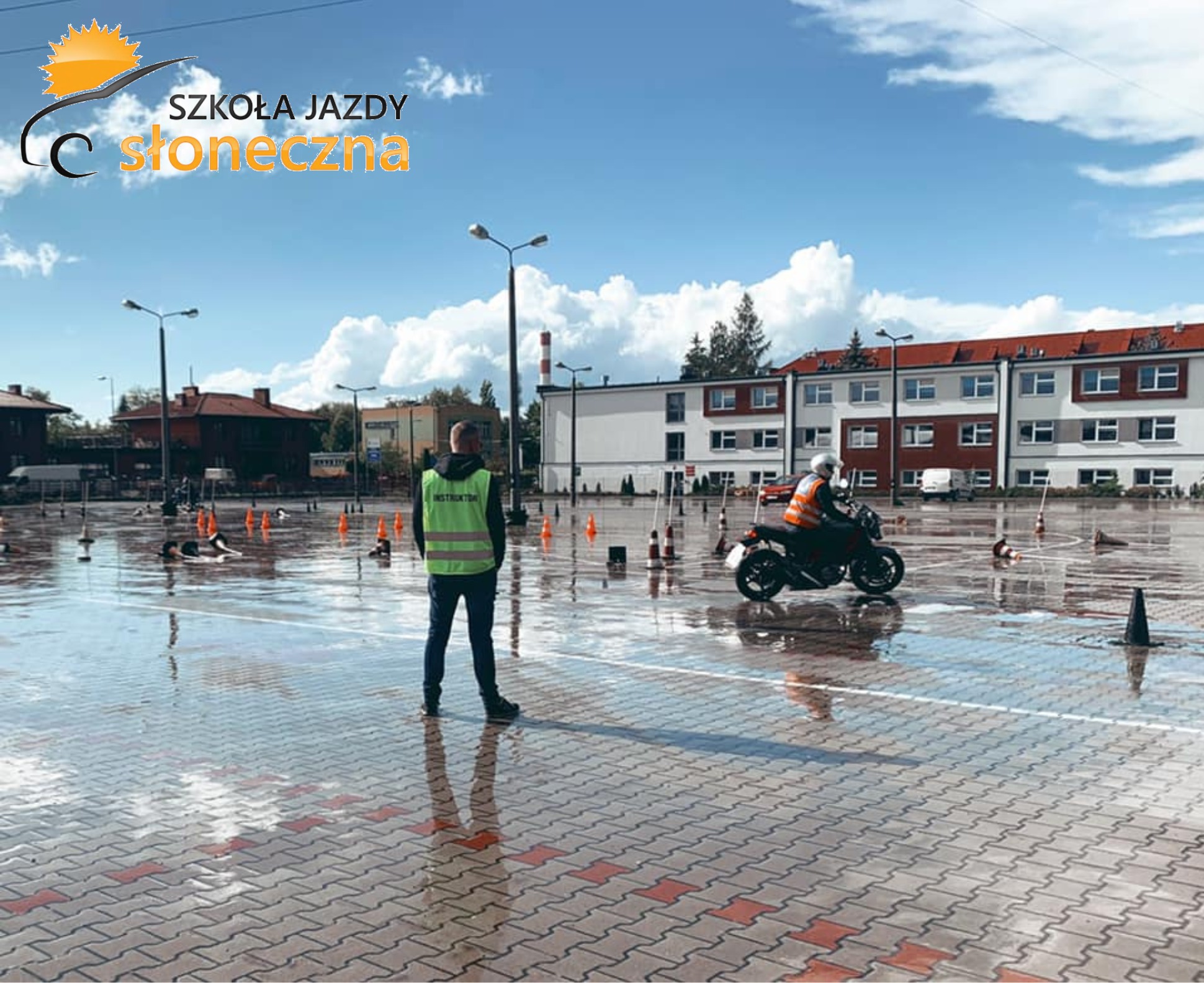Plac manewrowy po deszczu: instruktor w kamizelce obserwuje kursanta na motocyklu, widoczne pachołki.