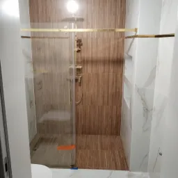 Nowoczesna kabina prysznicowa z elementami w kolorze złotym, drewnopodobne płytki pionowe na ścianie, marmurowe płytki na ścianach bocznych z wnękami.