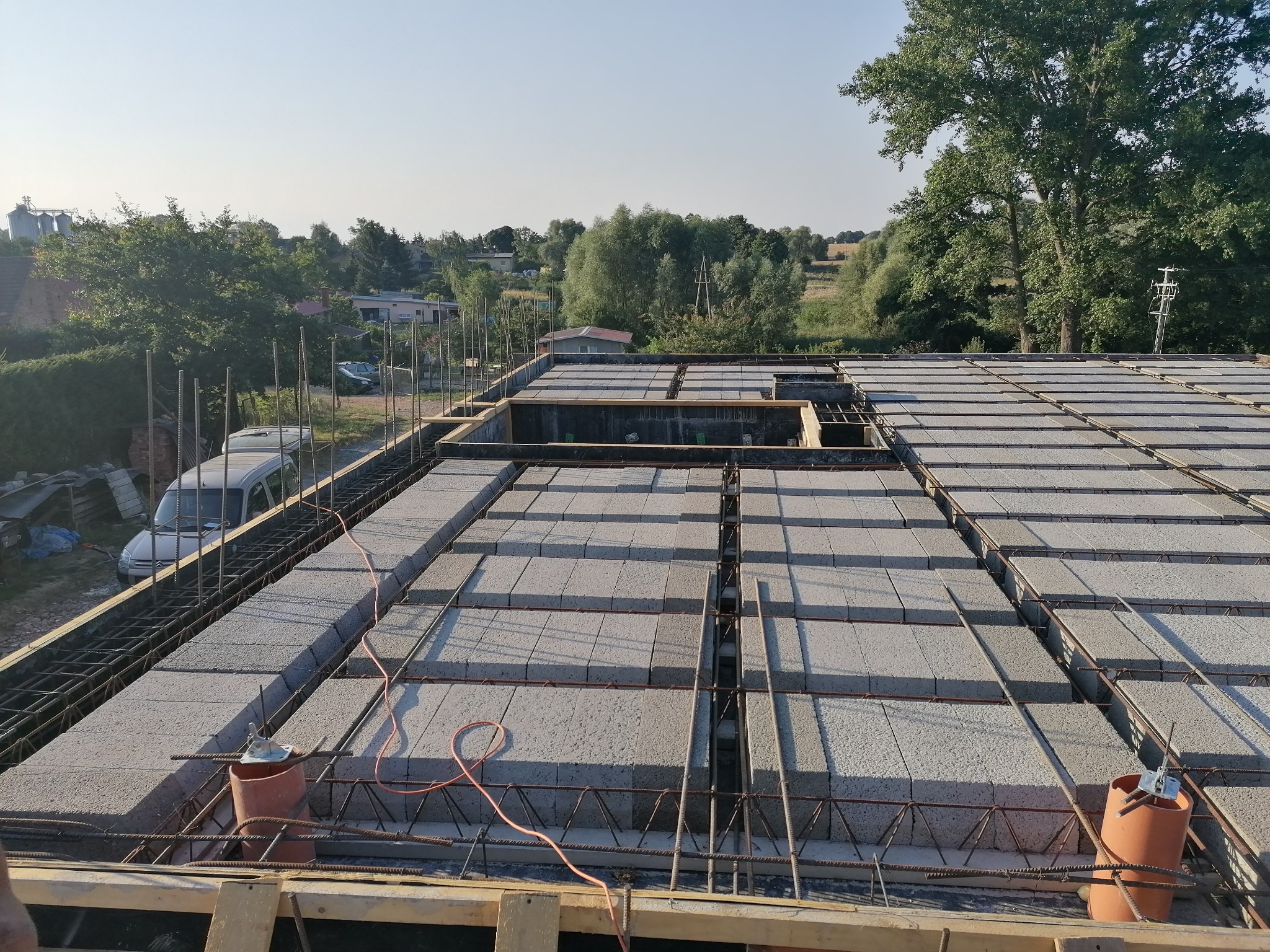 Budowa stropu Teriva: widok z góry na ułożone bloczki stropowe i zbrojenie, w tle zabudowa jednorodzinna i zieleń.