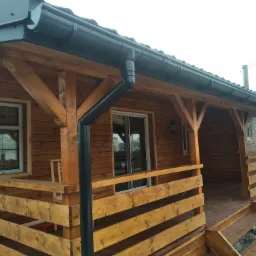 Zadaszony taras z drewnianą balustradą i czarnymi rynnami, widok z zewnątrz na jasny, pochmurny dzień.