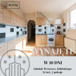 Jasna kuchnia z drewnianymi szafkami, białymi płytkami z czarnymi akcentami i marmurowym blatem, oświetlona naturalnym światłem z okna, z napisem 'Wynajęte' na pierwszym planie.