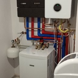 SERWIS GAZOWYCH URZĄDZEŃ GRZEWCZYCH -PAWEŁ ROKOSZ - Nowoczesny, biały piec gazowy Bosch z czarnym modułem sterującym i instalacją z rur miedzianych i izolowanych na niebiesko-czerwono, w kotłowni. Widoczny zbiornik wyrównawczy.