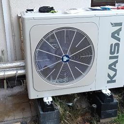 RP Gaz-Serwis - Biała pompa ciepła Kaisai zamontowana na zewnątrz budynku, z otwartym panelem elektrycznym i widocznymi narzędziami, na tle elewacji i trawy.