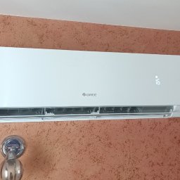 RP Gaz-Serwis - Biała jednostka wewnętrzna klimatyzatora GREE zamontowana na ścianie o rdzawobrązowej, fakturowanej powierzchni, z widocznym cyfrowym wyświetlaczem '16'.
