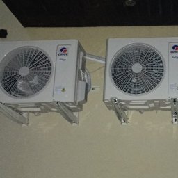 RP Gaz-Serwis - Dwie białe jednostki zewnętrzne klimatyzacji GREE z widocznymi wentylatorami, zamontowane na jasnej ścianie pod ciemnym sufitem z balustradą.
