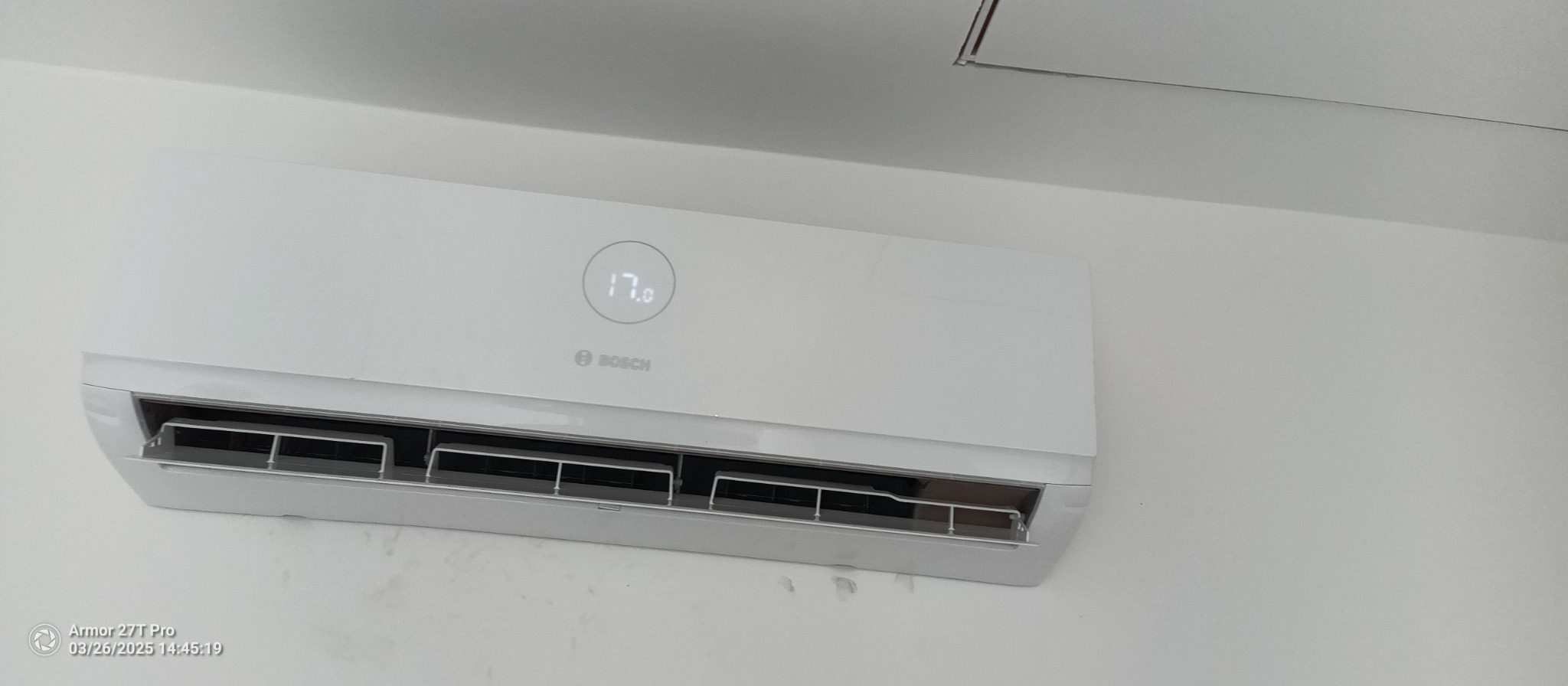 Biały klimatyzator Bosch zamontowany na ścianie, ustawiony na 17 stopni Celsjusza. Widoczne żaluzje wylotowe i fragment sufitu.