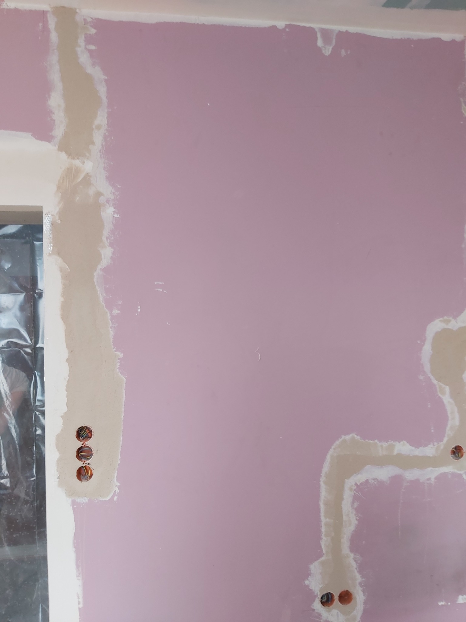 Różowa ściana z widocznymi puszkami elektrycznymi przed malowaniem, z widocznymi śladami po szpachlowaniu wokół przewodów.