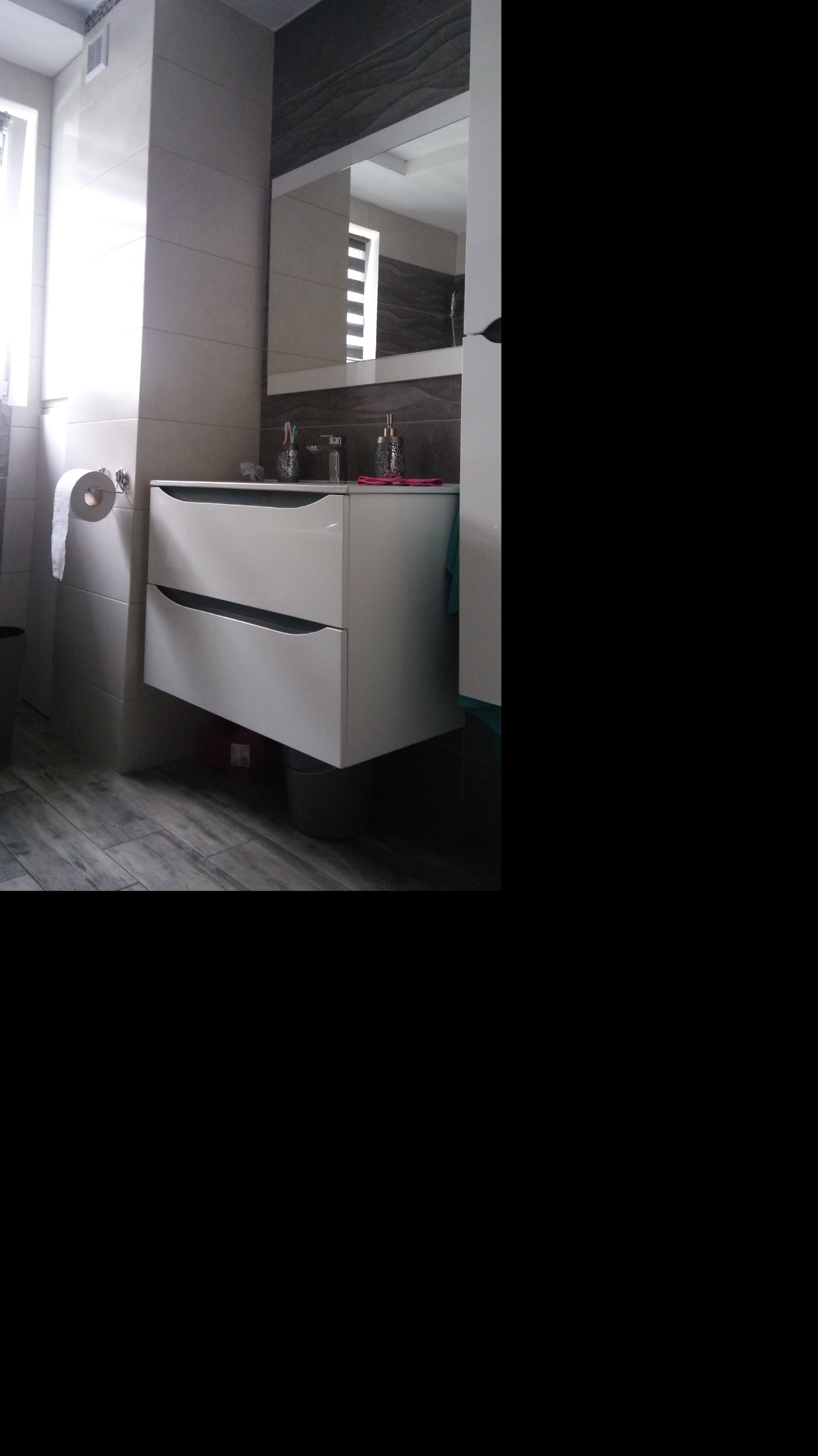 Nowoczesna łazienka z białą, podwieszaną szafką umywalkową, szarą glazurą imitującą drewno i dużym lustrem.