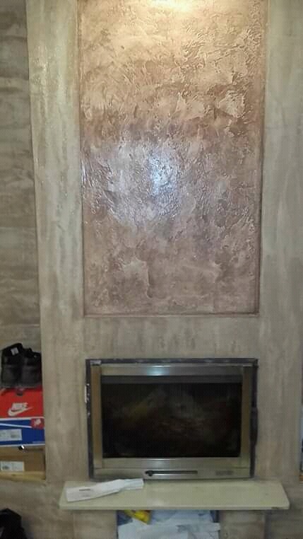 Dekoracyjna ściana z efektem stiuku w odcieniach beżu i brązu nad kominkiem, z widocznymi pudełkami po butach w tle.