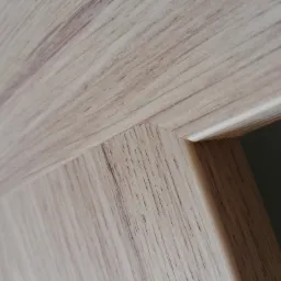 Fragment drewnianej ramy drzwi wewnętrznych z widocznym usłojeniem, o jasnym odcieniu drewna, w minimalistycznym stylu.