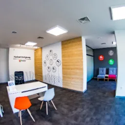 Jasne biuro z drewnopodobną okładziną ścienną, minimalistycznymi meblami i grafikami informacyjnymi na ścianach.