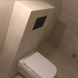 Podwieszana toaleta z zabudową geberit w beżowej, wykafelkowanej łazience, z widocznym czarnym przyciskiem spłukującym.