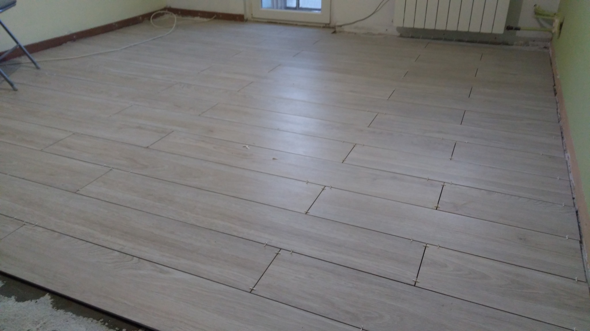 Układanie podłogi z płytek imitujących drewno z użyciem krzyżyków dystansowych, widoczne niedociągnięcia przy ścianie.