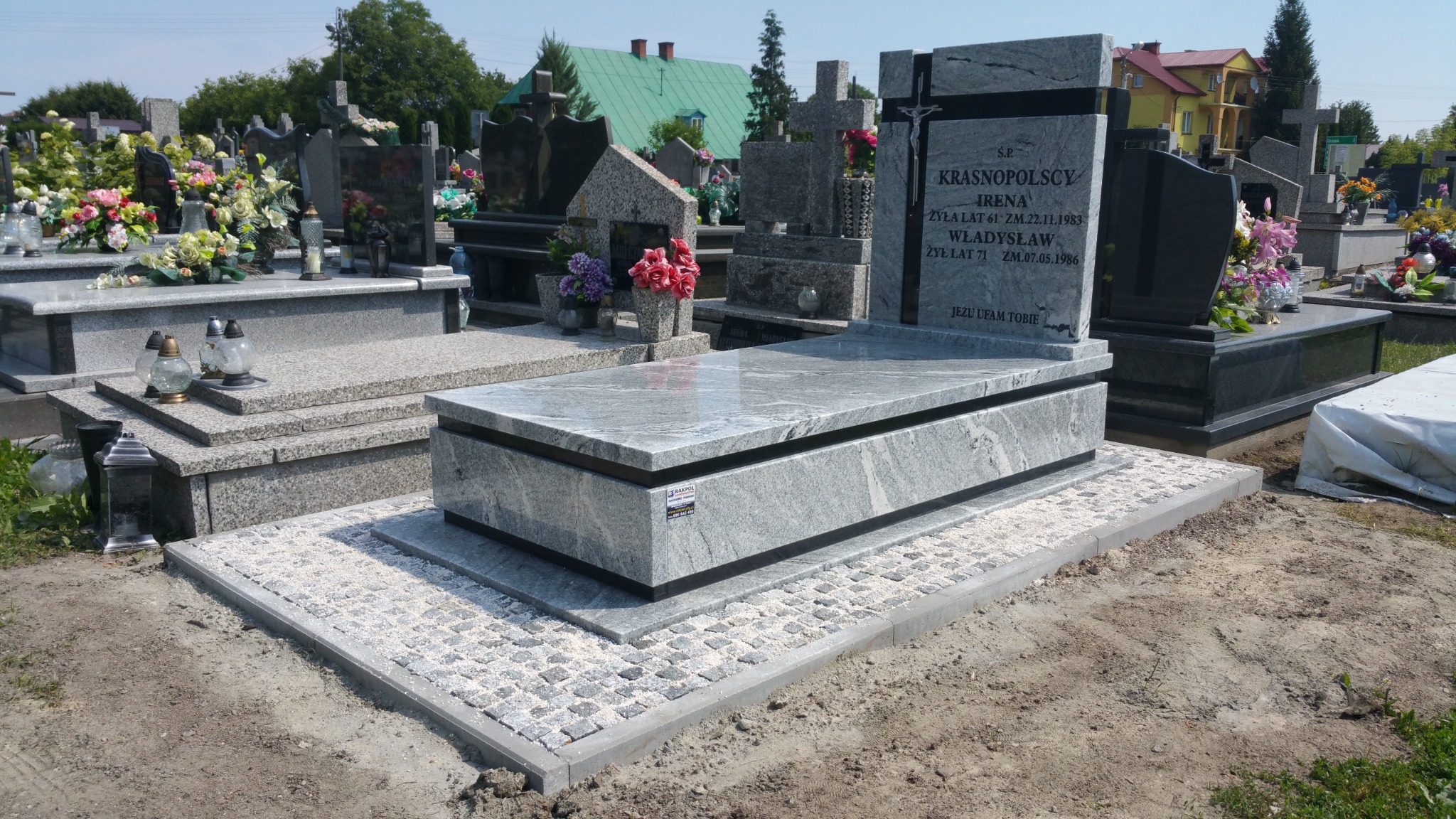 Jasnoszary, nowoczesny nagrobek z kamienia Indie Viscont White na cmentarzu, otoczony kostką brukową i innymi nagrobkami.