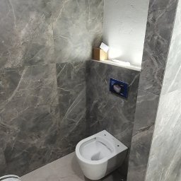 G&K Stroi - Montaż podwieszanej miski WC na tle szarej ściany imitującej marmur, widoczny pojemnik z masą szpachlową i fragment listwy przypodłogowej.