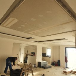 G&K Stroi - Montaż podwieszanego sufitu z płyty kartonowo-gipsowej w przestronnym, remontowanym wnętrzu z widocznymi elementami konstrukcyjnymi i pracującym mężczyzną.