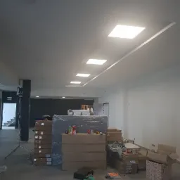 Montaż sufitu z wbudowanymi panelami LED w trakcie prac wykończeniowych, widoczne materiały budowlane i narzędzia na podłodze.