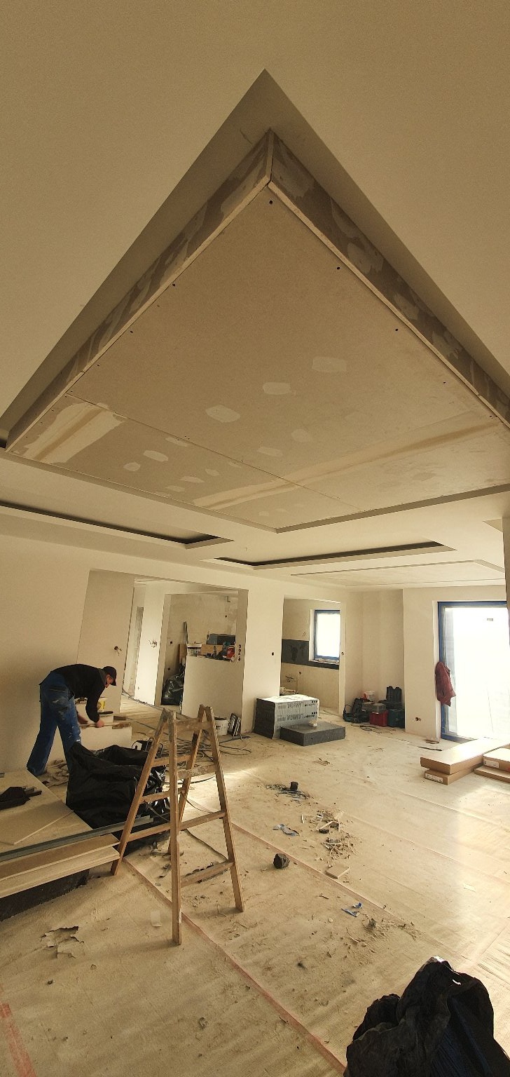 Montaż podwieszanego sufitu z płyty kartonowo-gipsowej w przestronnym, remontowanym wnętrzu z widocznymi elementami konstrukcyjnymi i pracującym mężczyzną.