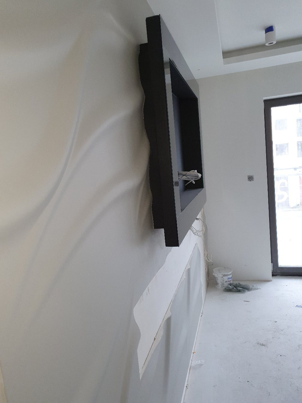 Montaż dekoracyjnej ramy ściennej z czarnym obramowaniem, widoczne przygotowane ściany i fragment instalacji elektrycznej, surowe wykończenie wnętrza.